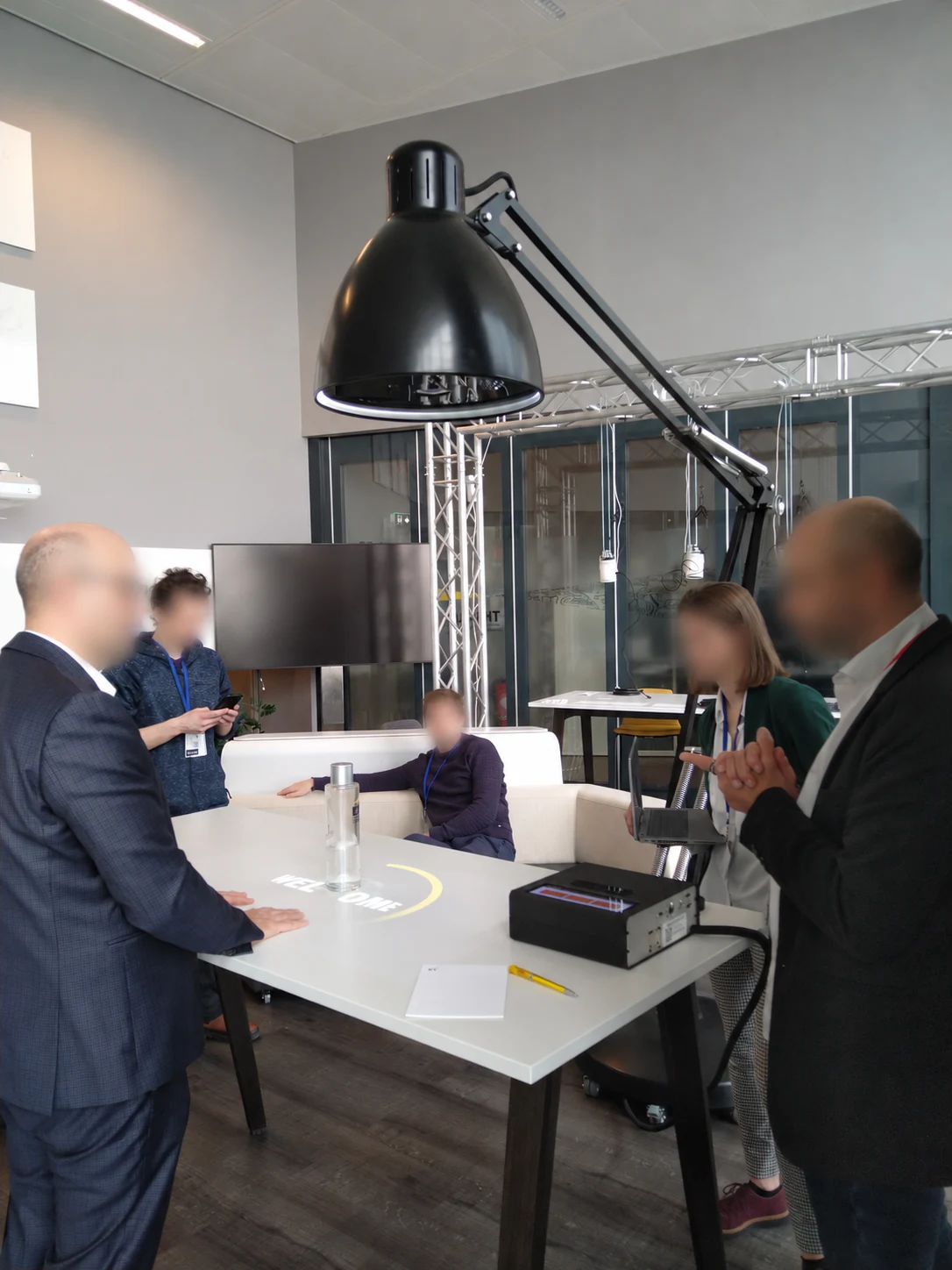 Participants autour de la lampe interactive EY et de sa table de projection dans une salle lumineuse, visages floutés
