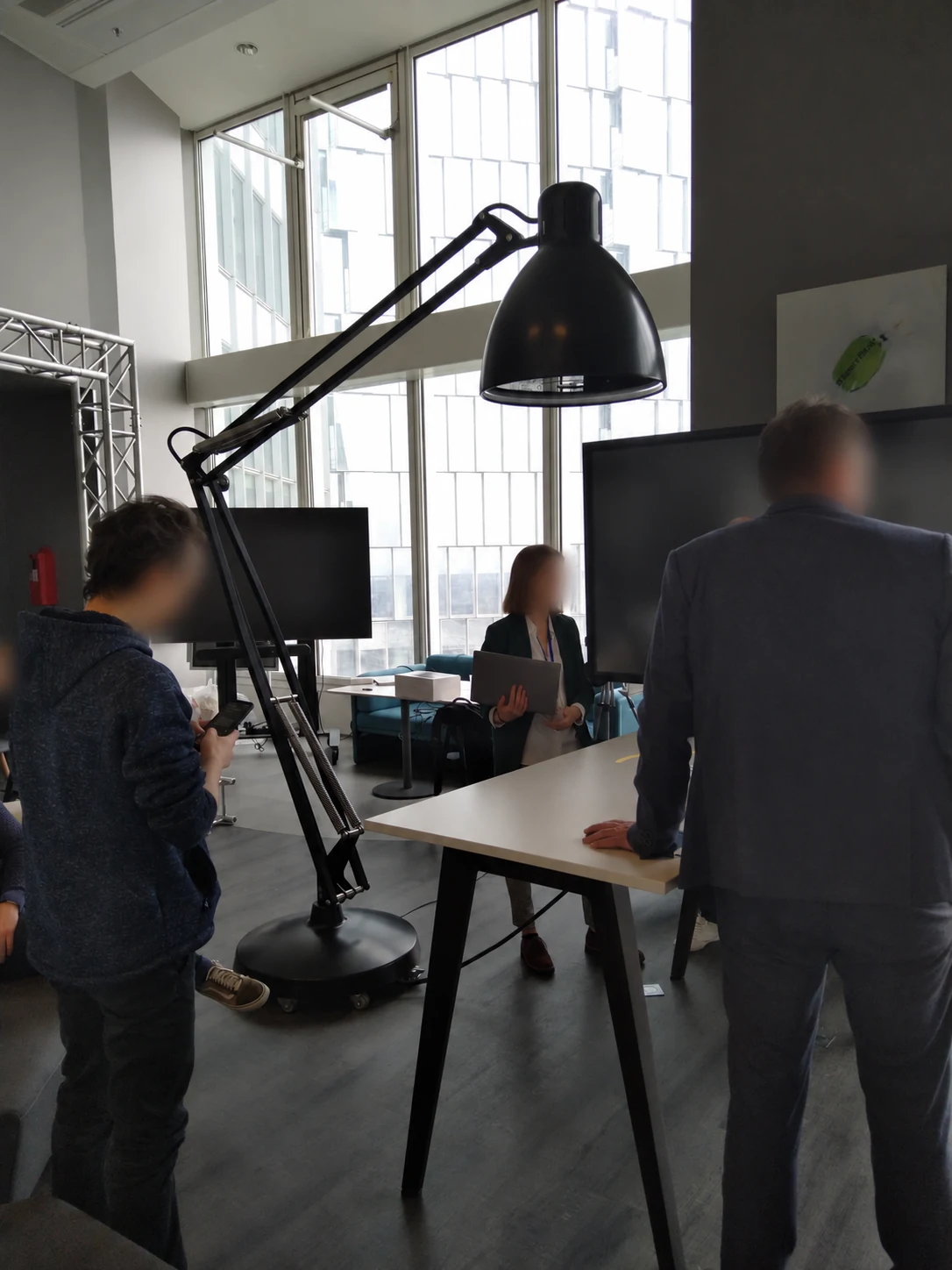 Lampe interactive EY à bras articulé noir au-dessus d’une table, avec des visiteurs dont les visages sont floutés