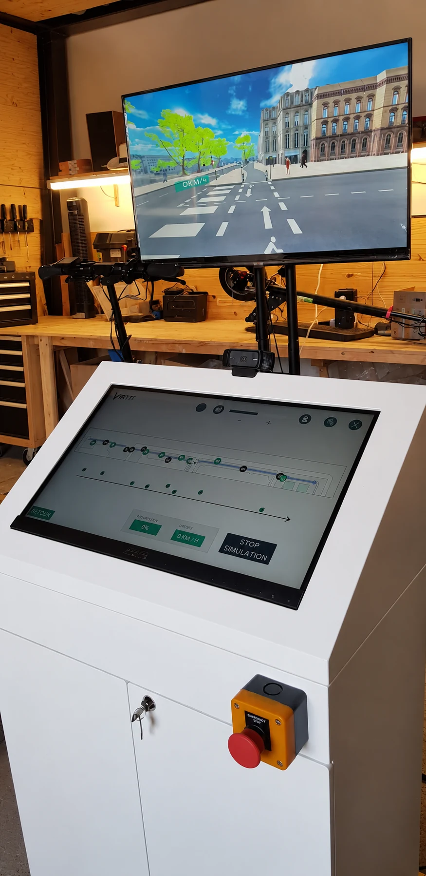 Borne tactile blanche affichant l’interface de pilotage, sous un écran de simulation, dans un atelier