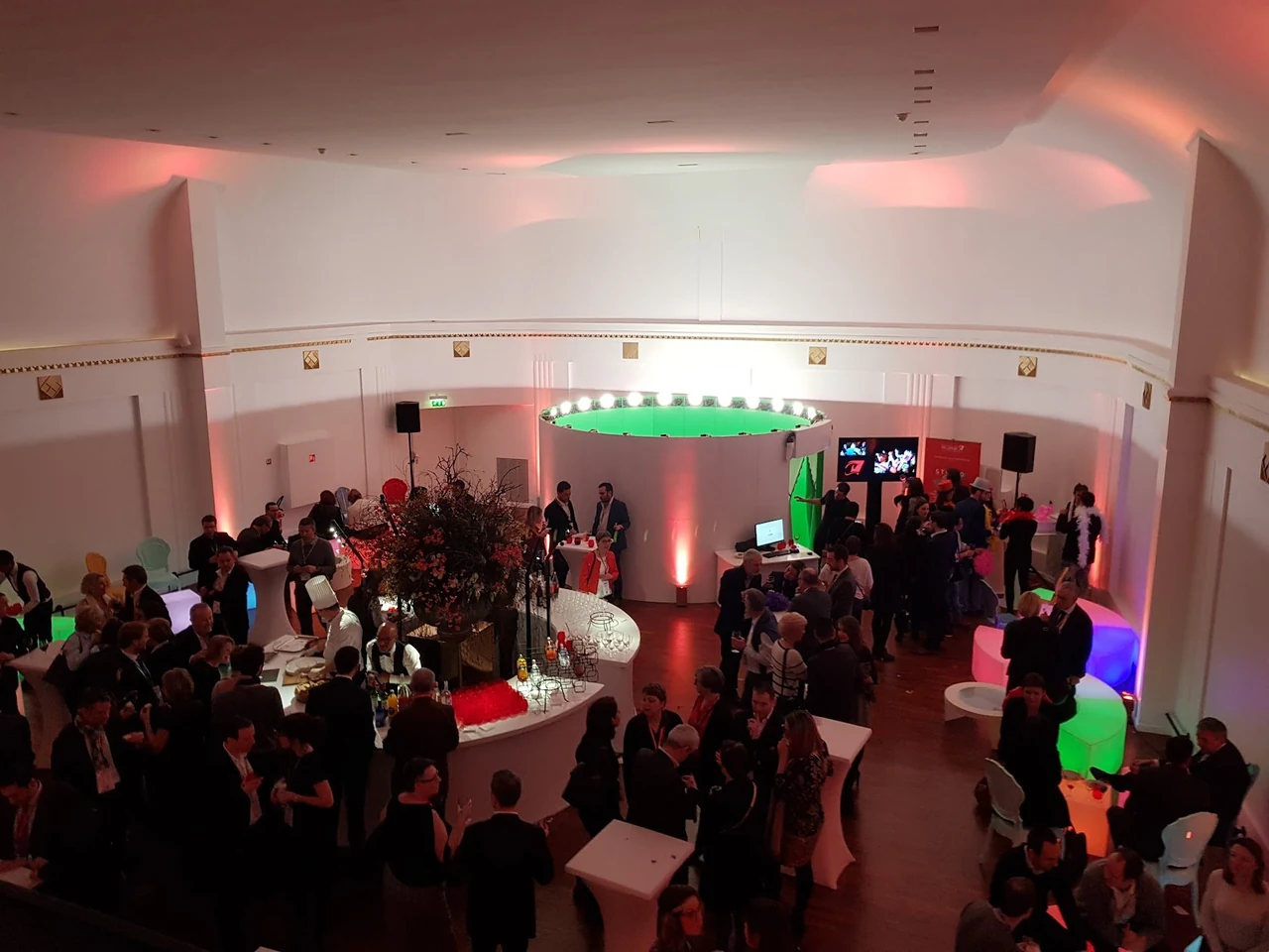 Foule dans une salle d’événement éclairée de rouge, autour du studio à fond vert installé au centre