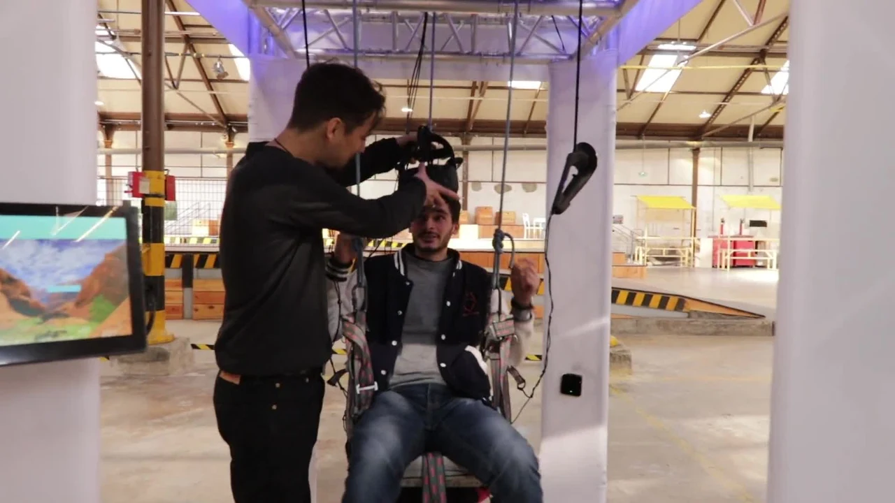 Une personne près d’un utilisateur équipé d’un casque VR et assis dans la nacelle, dans un grand hall