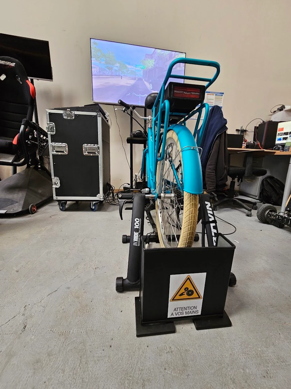 Vélo bleu monté sur son support d’entraînement, avec écran en arrière-plan, dans un atelier