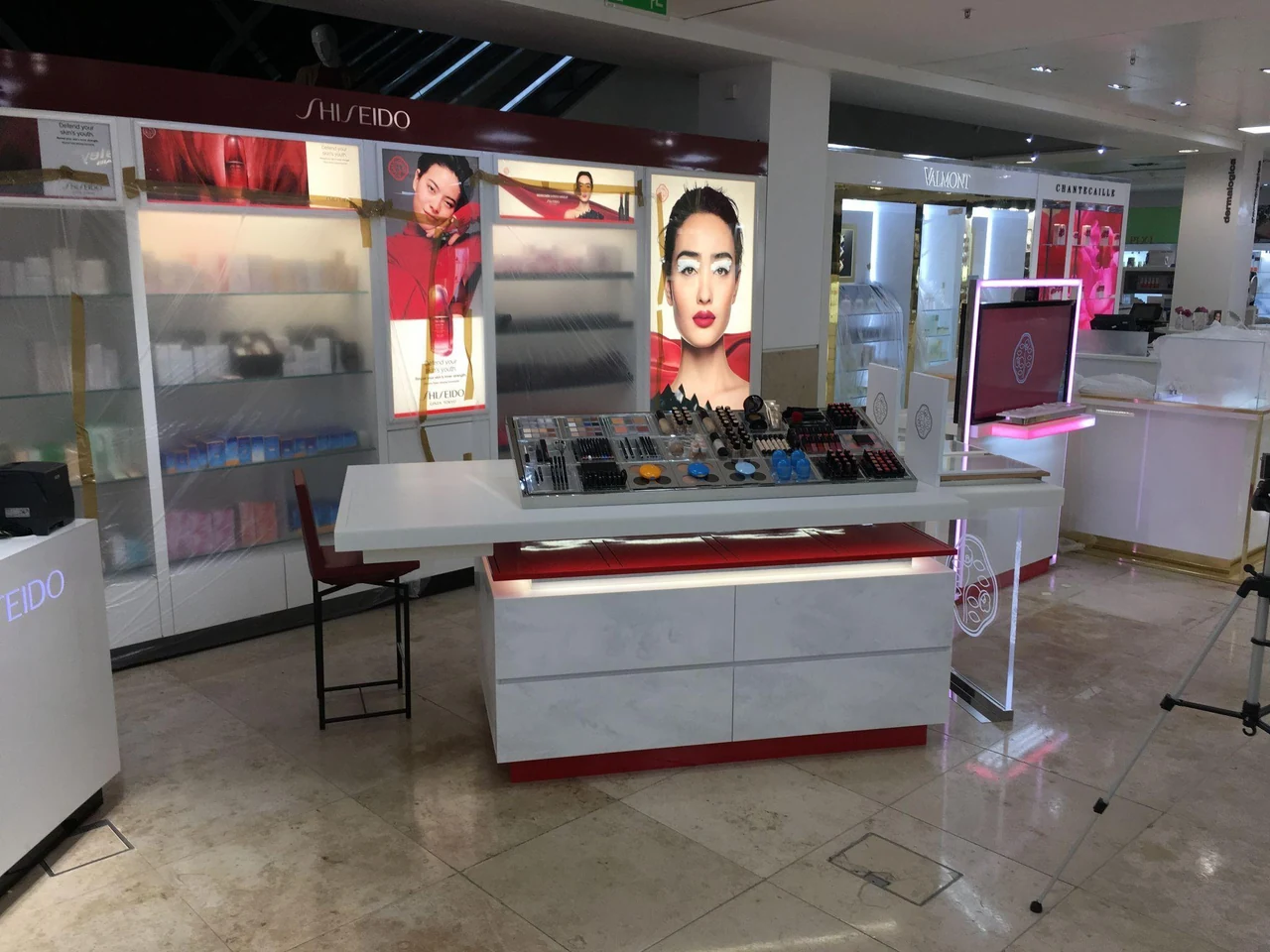 Comptoir de présentation de produits de beauté dans un espace de vente, avec affiches et écrans lumineux