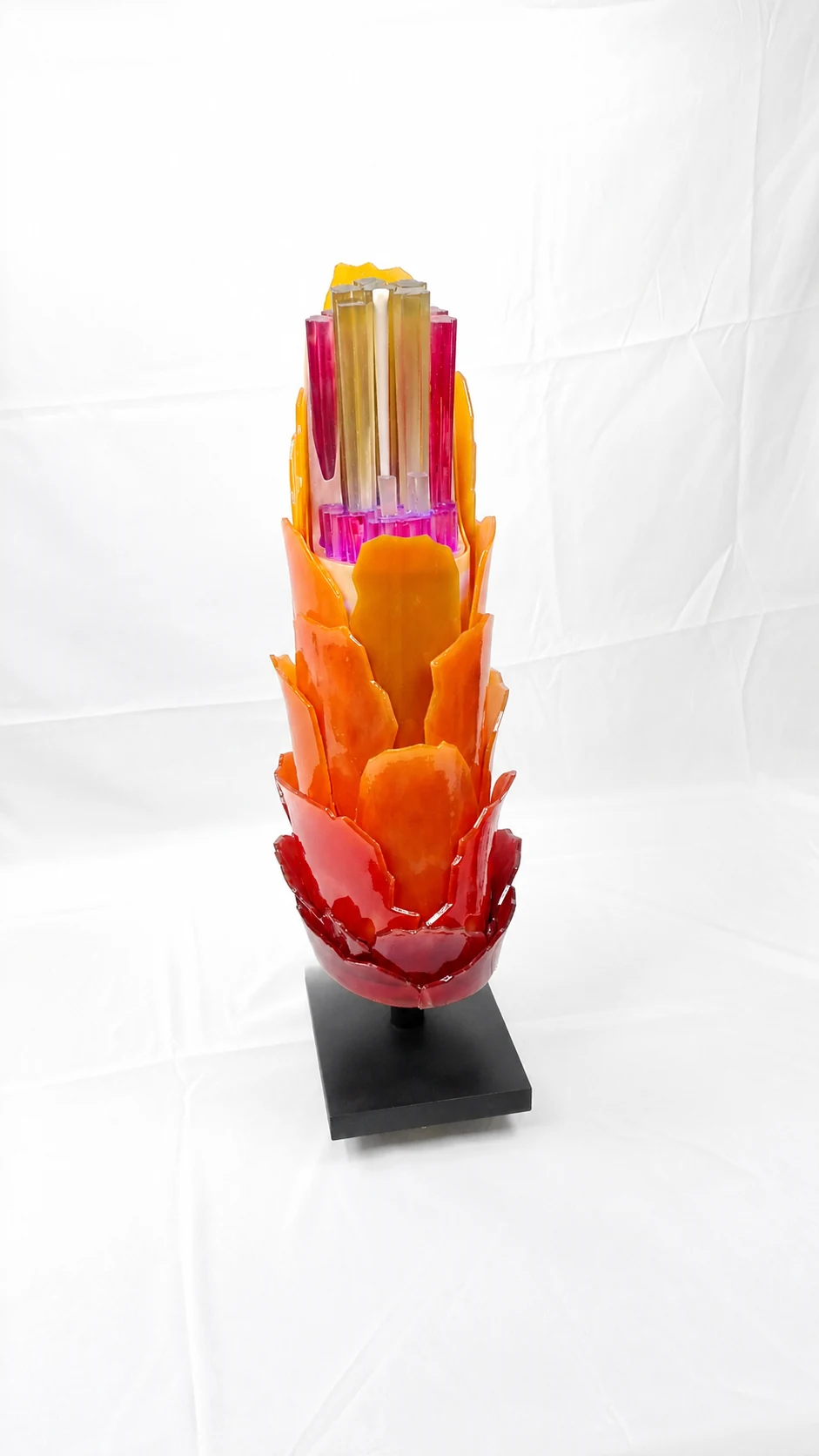 Sculpture à couches rouges et orange sur un socle noir, sur fond blanc