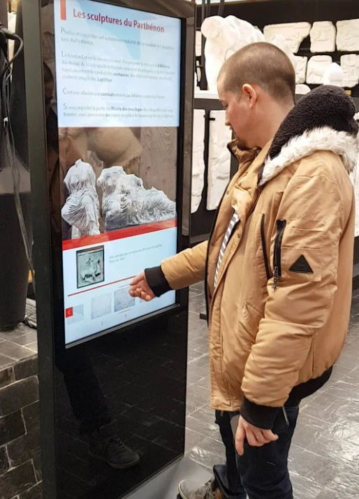 Visiteur utilisant un grand écran tactile vertical qui affiche une sculpture numérisée