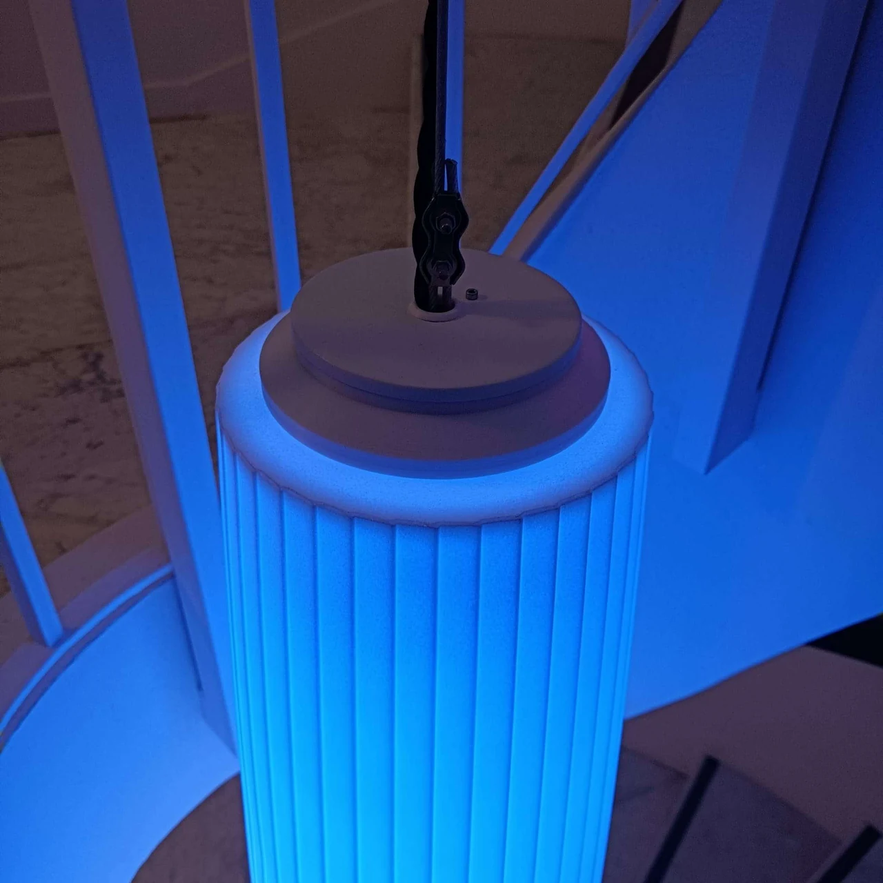 Bas du lustre éclairé en bleu turquoise, suspendu par son câble au-dessus de l’escalier