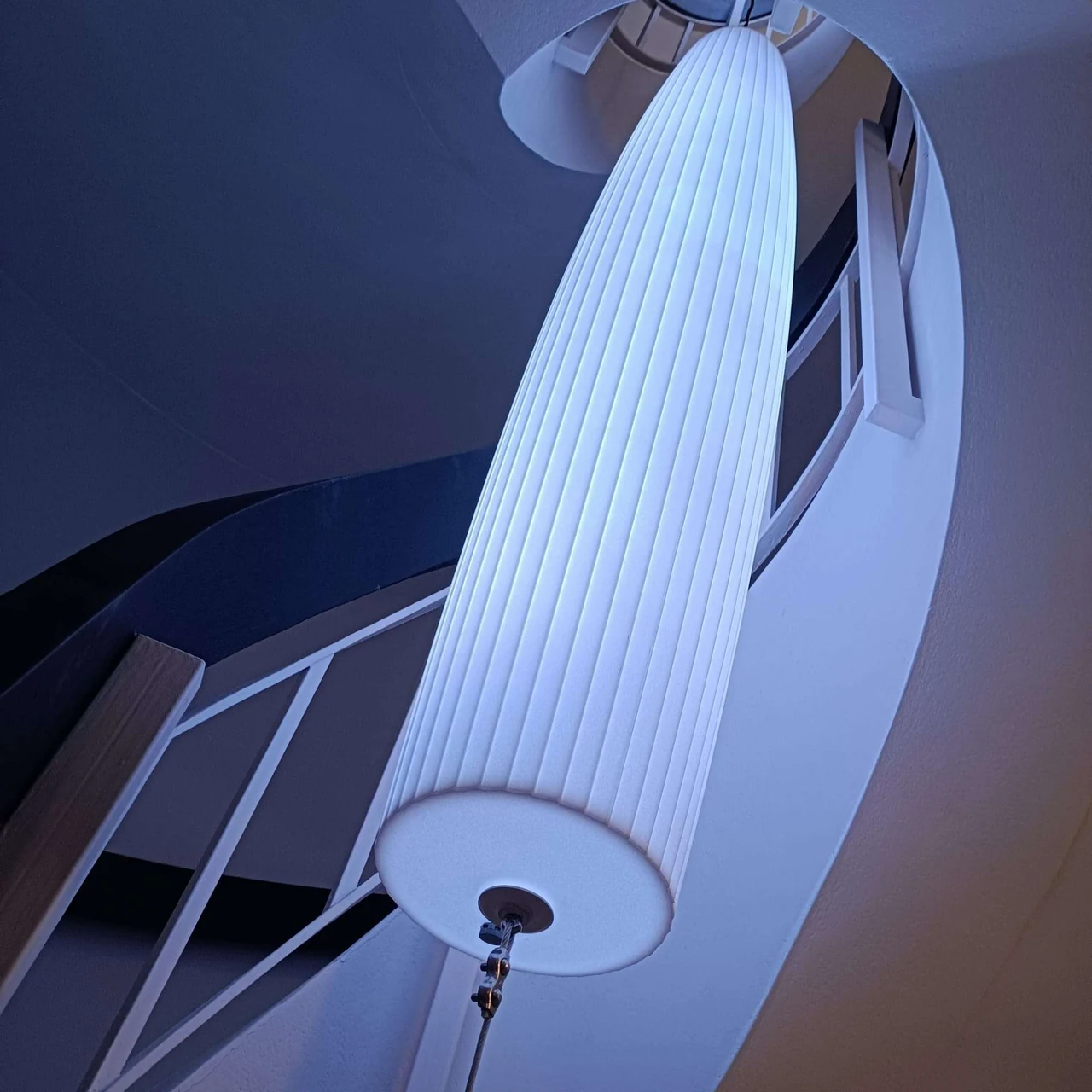 Lustre blanc incliné dans l’escalier, éclairé en bleu clair