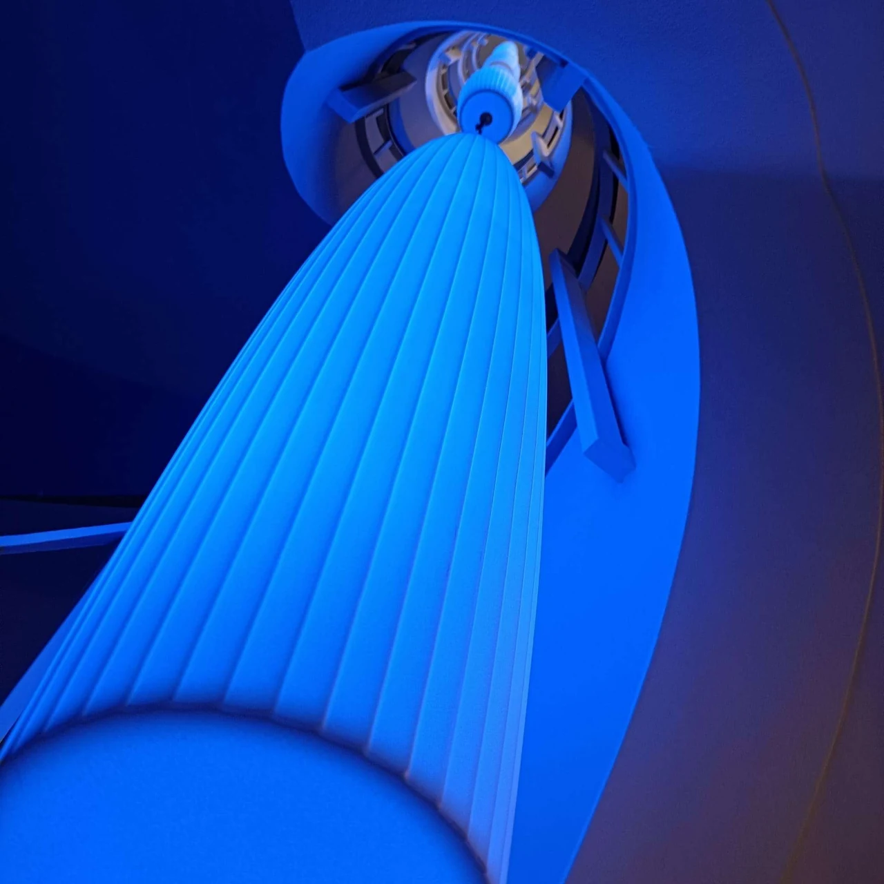 Lustre éclairé en bleu intense, vu d’en dessous, avec les marches de l’escalier derrière