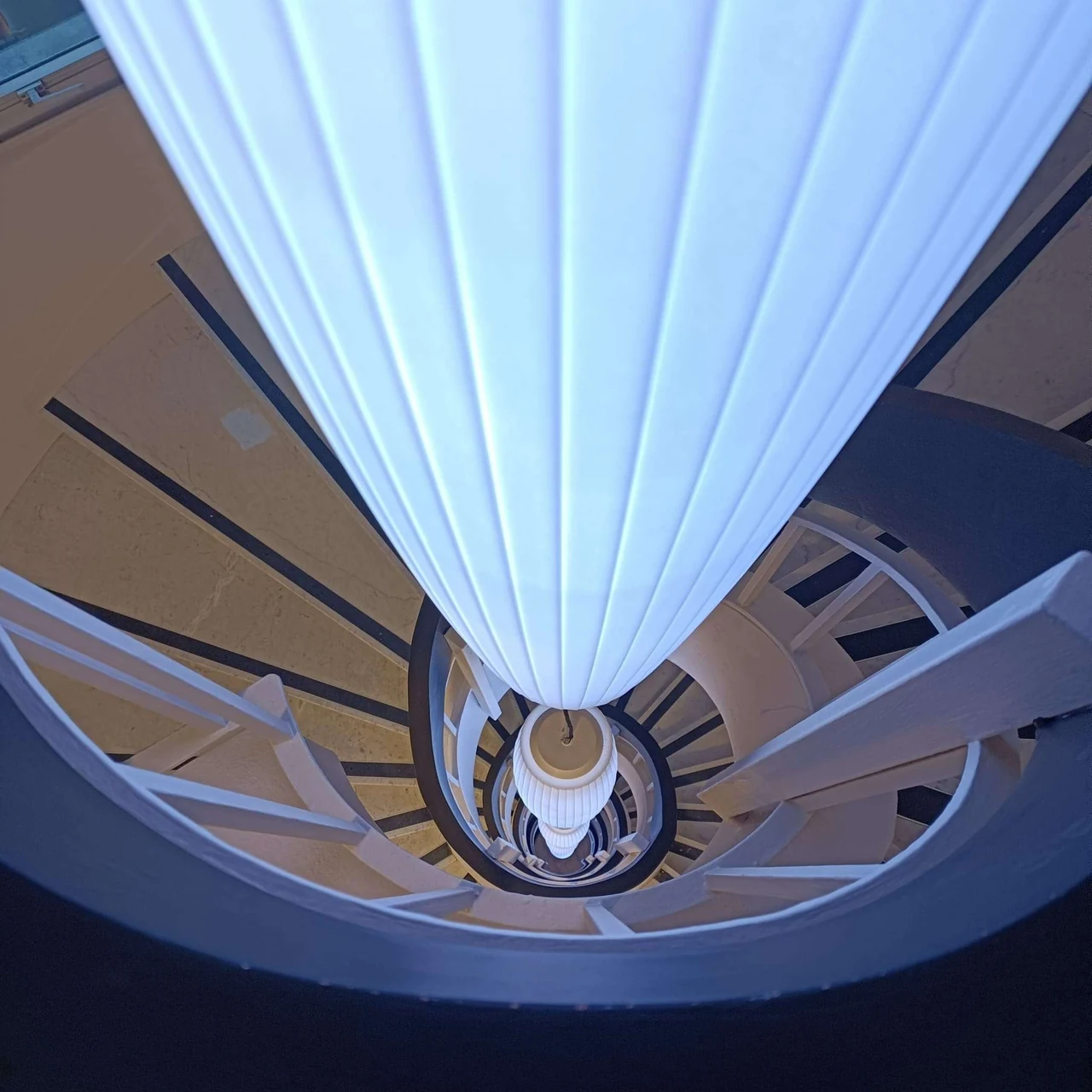 Lustre blanc cannelé vu d’en dessous, avec l’escalier en spirale en perspective