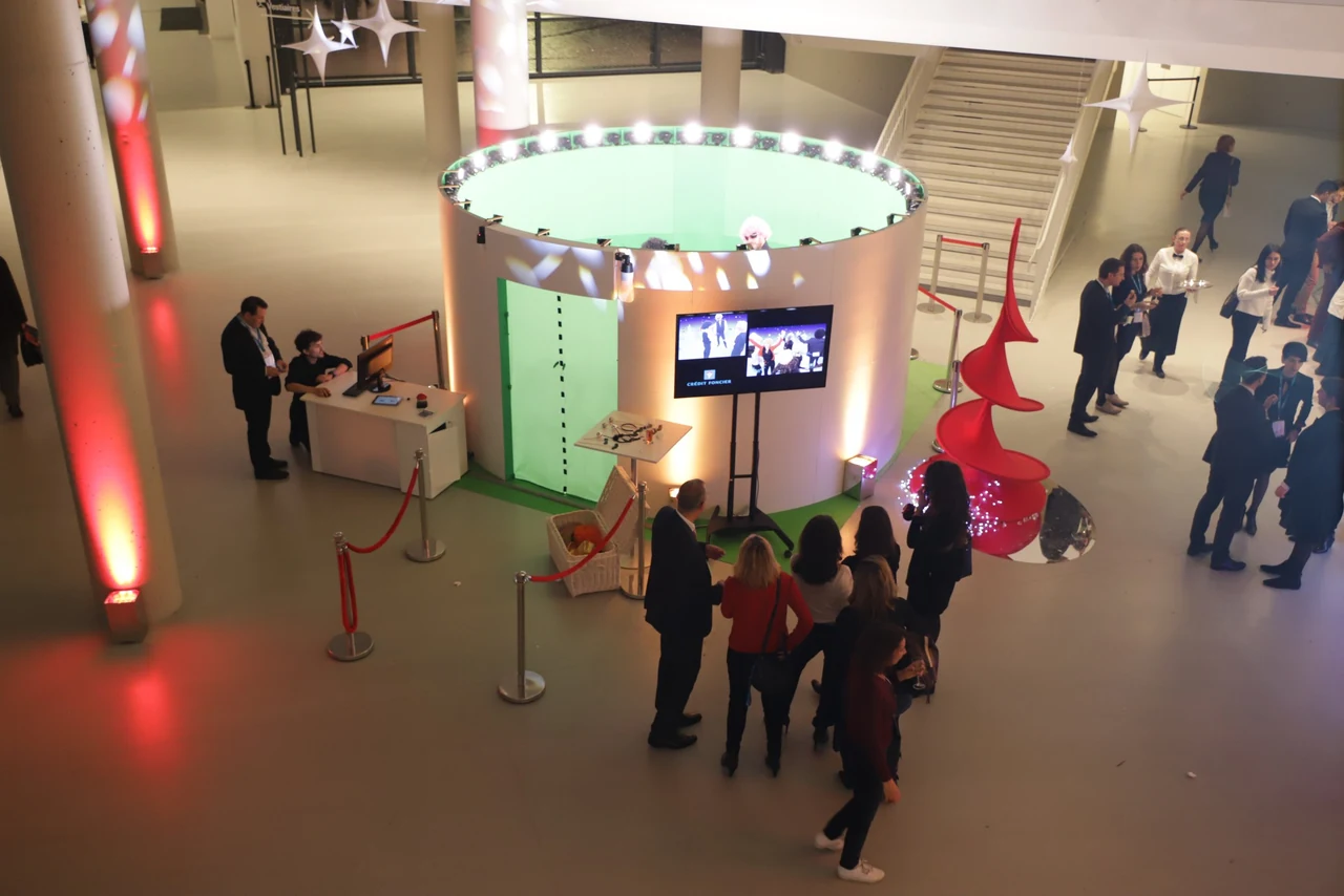Vue en plongée d’un hall d’événement avec le studio Bullet Time, un socle circulaire blanc à couronne lumineuse, et des visiteurs