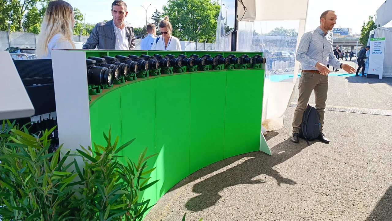 Mur courbe à fond vert surmonté d’appareils photo, avec une personne debout en extérieur