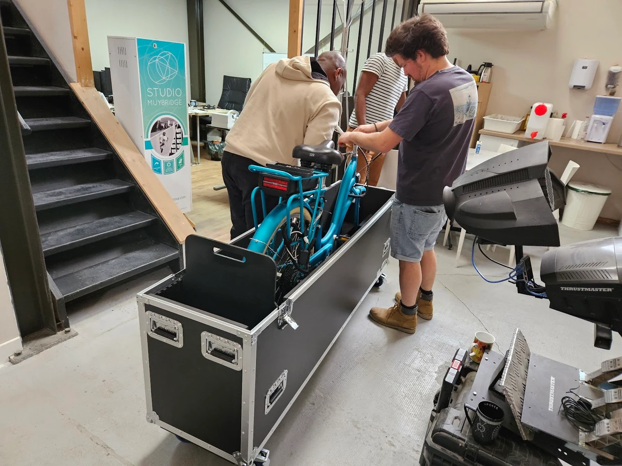 Deux personnes près d’un vélo bleu dans un flycase ouvert, au pied d’un escalier